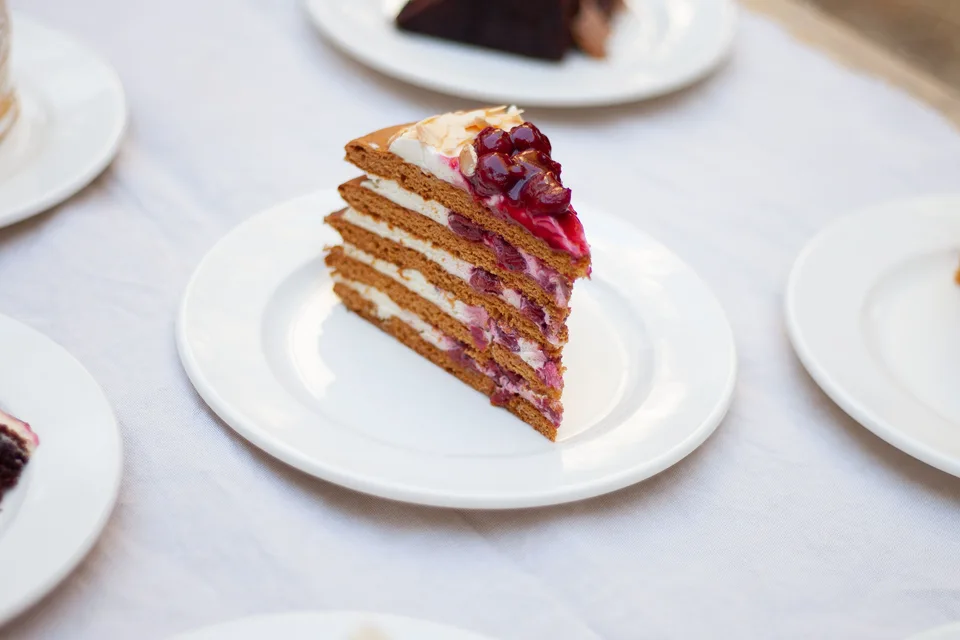 Primer fotografije: Rezina večplastne torte, okrašena z jagodami, na belem krožniku