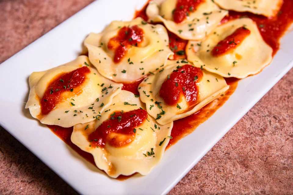 Primer fotografije: Ravioli s paradižnikovo omako in zelišči na belem krožniku